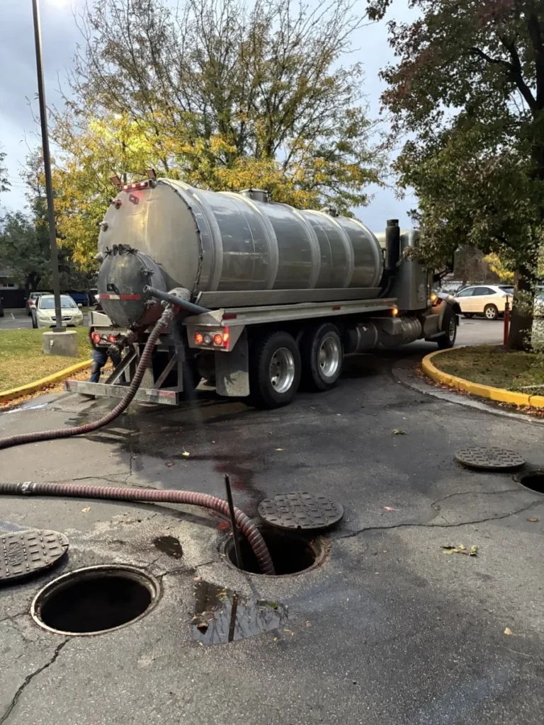 Vacuum pump truck with suction hoses run to open grease interceptor access points in a parking lot