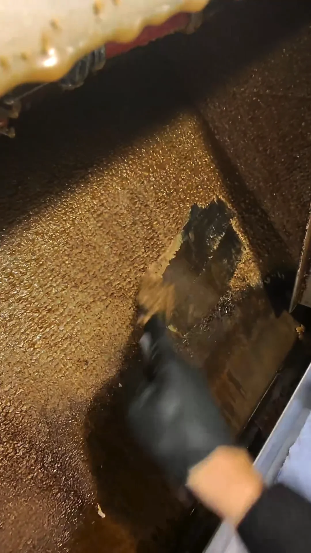 Gloved hand scraping thick grease buildup from a hood surface