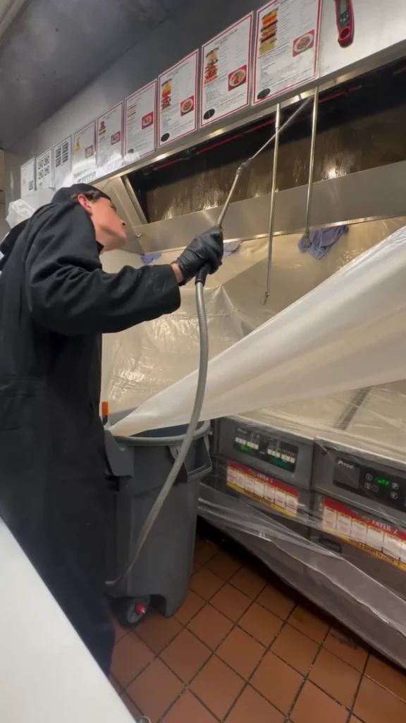 Technician spraying degreaser on a kitchen exhaust hood
