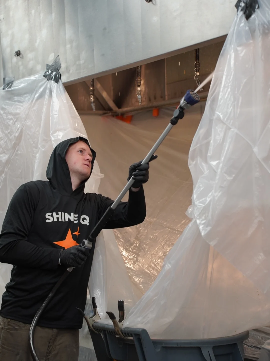 Technician spraying a plastic-wrapped kitchen hood in a stadium concession kitchen