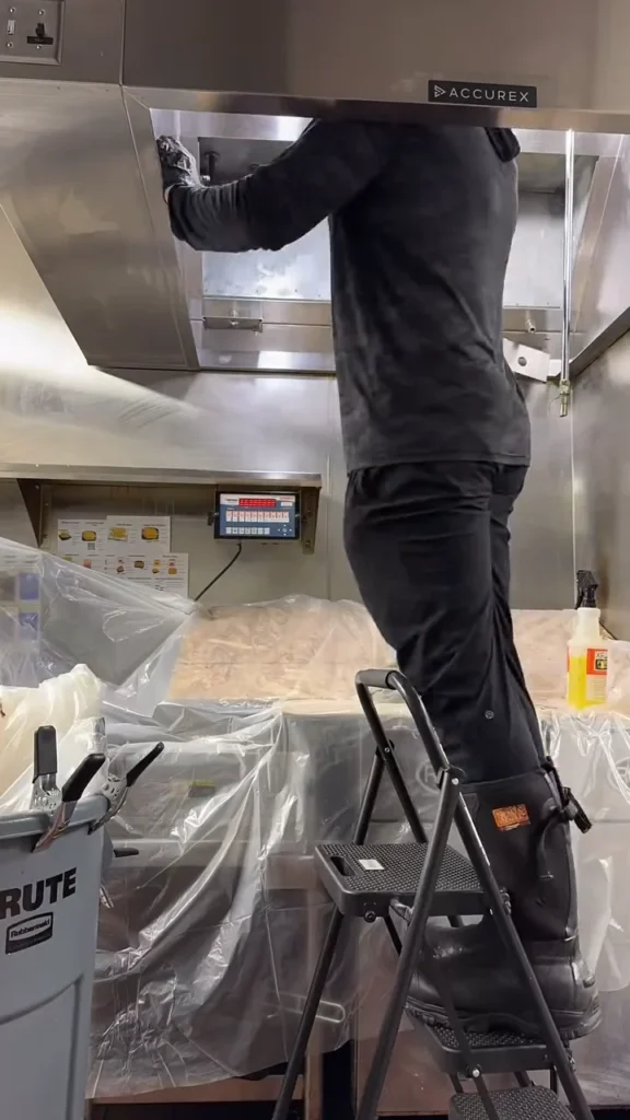 Technician on a ladder cleaning a wrapped kitchen hood