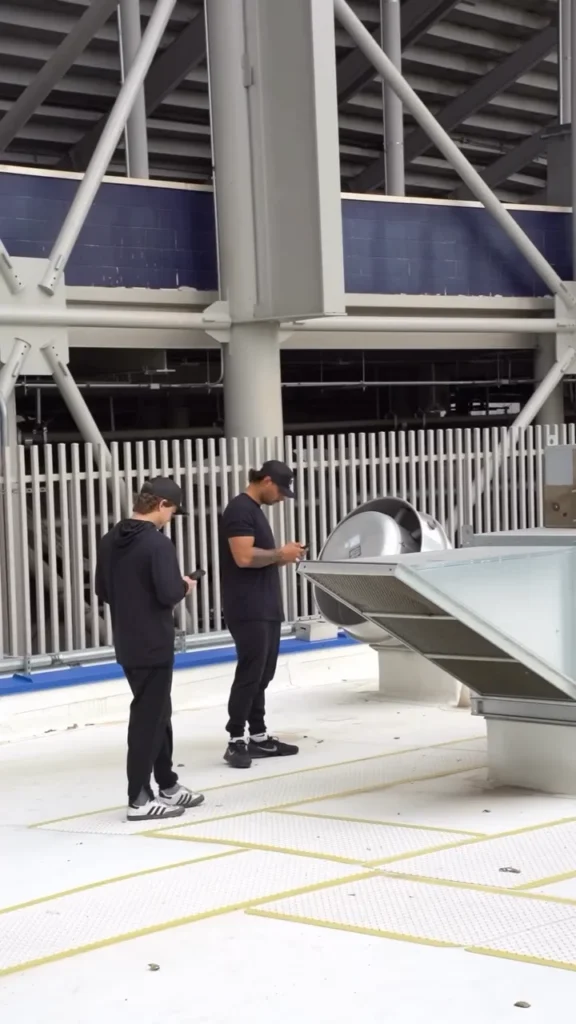 Two technicians beside an exhaust fan on a stadium concourse