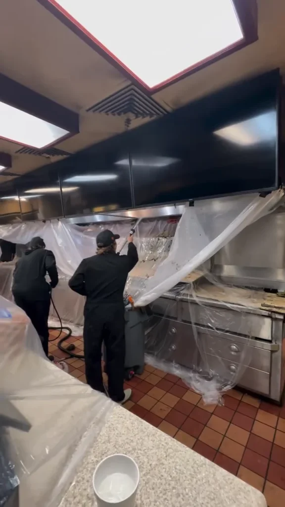 Two technicians working under a wrapped commercial kitchen hood line