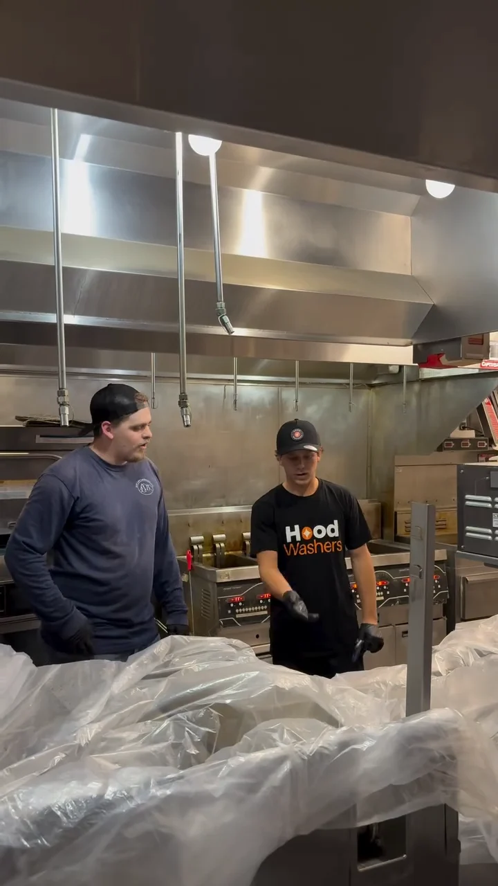 Two technicians wrapping kitchen equipment in plastic before a hood cleaning